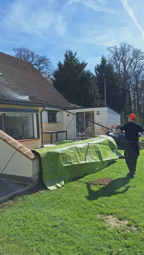 Démoussage de toiture à la perche télescopique depuis le sol, jardin protégé par une bâche