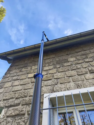 Nettoyage de gouttière à la perche télescopique sur une maison en pierre